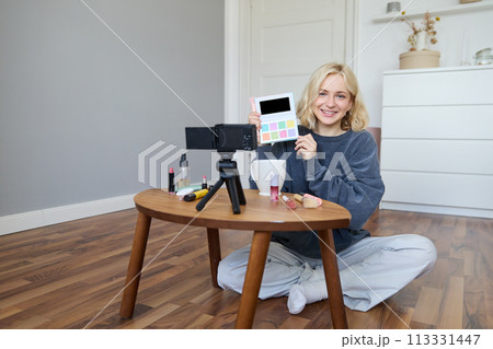 Portrait of beautiful smiling woman, recording video in her room, has camera on coffee table, reviewing makeup, doing lifestyle vlog for social media account, records a tutorial 113331447