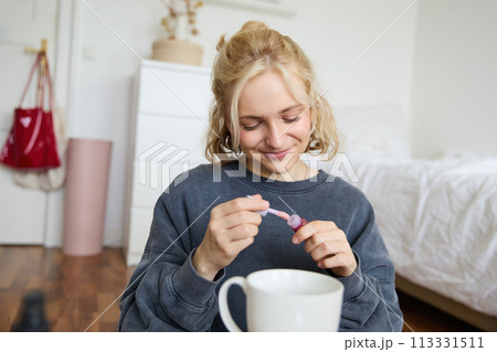 Portrait of smiling charismatic woman, puts on lip gloss, drinks tea, records video on digital camera, beauty content for social media account Portrait of smiling charismatic woman, puts on lip gloss, drinks tea, records video on digital camera, beauty content for social media account 113331511