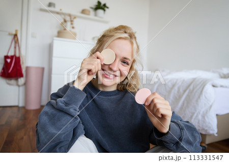 Portrait of young woman chatting on live stream about makeup, sits on floor in bedroom, showing beauty products to followers Portrait of young woman chatting on live stream about makeup, sits on floor in bedroom, showing beauty products to followers 113331547