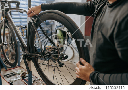 Close up of man working in a bicycle repair shop and checking the wheel of the bike Close up of man working in a bicycle repair shop and checking the wheel of the bike 113332313