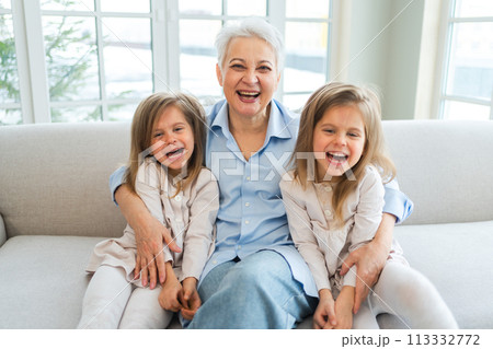Happy family at home. Two little girls sisters twins grandmother enjoying time together. Good time at home. Grandma granddaughters child kids emotional bonding hugging together. Family generations 113332772