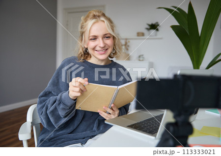 Portrait of young woman using digital camera and laptop, studying, connect to online live stream, records video for vlog, creating content, holding notebook, sitting in room Portrait of young woman using digital camera and laptop, studying, connect to online live stream, records video for vlog, creating content, holding notebook, sitting in room 113333021