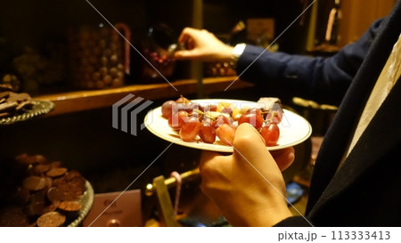 A person is holding a plate with grapes and a piece of cheese. A person is holding a plate with grapes and a piece of cheese. 113333413