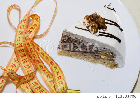 piece of a chocolate cake wrapped with a yellow measuring tape diet and healthy living concept image. 113333786