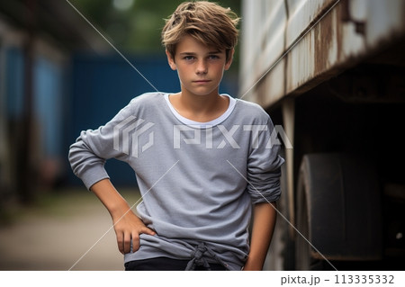 A young boy stands in front of a truck, wearing a gray shirt and black pants A young boy stands in front of a truck, wearing a gray shirt and black pants 113335332