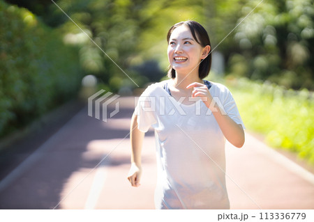 スポーツウエアでランニングをする笑顔の若い女性 スポーツウエアでランニングをする笑顔の若い女性 113336779