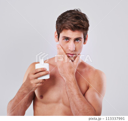 Young man, portrait and aftershave with cosmetics for skincare or lotion on a gray studio background. Face of handsome male person or model with beauty creme or container for hygiene on mockup space Young man, portrait and aftershave with cosmetics for skincare or lotion on a gray studio background. Face of handsome male person or model with beauty creme or container for hygiene on mockup space 113337991