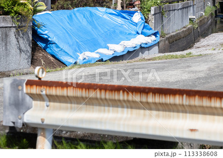 自然災害で被害が出ている民家　崩れた部分にブルーシートと土嚢が置かれている 113338608