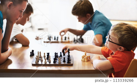 Chess whiz. Young boy wearing spectacles and playing chess with an older child. 113339266