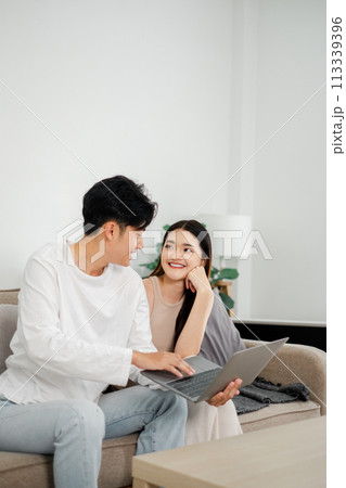 Young couple shares a joyful moment while looking at a laptop together on a cozy couch in a bright living room. 113339396