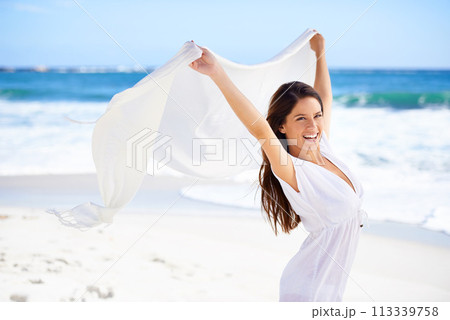 Portrait, happy woman and fabric in wind at beach outdoor for summer, vacation and travel on holiday. Ocean, smile and person fly with scarf in the air for adventure, freedom and sea breeze by water 113339758