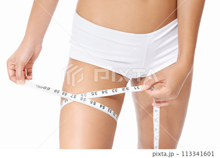 Woman, legs and tape measure for diet, weight loss or slim body in health and wellness on a white studio background. Closeup of female person or model hands measuring thigh in fitness or healthcare Woman, legs and tape measure for diet, weight loss or slim body in health and wellness on a white studio background. Closeup of female person or model hands measuring thigh in fitness or healthcare 113341601