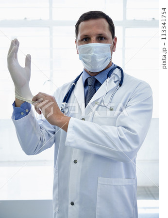 Portrait, doctor and putting on gloves in mask for protection or safety in hospital. Face, medical professional and man with ppe to prepare for surgery, treatment or prevention of disease for health Portrait, doctor and putting on gloves in mask for protection or safety in hospital. Face, medical professional and man with ppe to prepare for surgery, treatment or prevention of disease for health 113341754