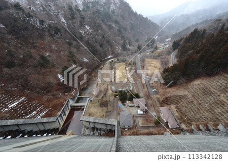 雪が降る四万川ダムの堤体と日向見公園、四万温泉街方面の景色 113342128