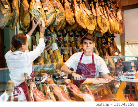 Cheerful young woman and man selling ham in jamoneria 113343159