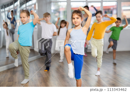 Positive juvenile girl engaged in hip-hop dance in training room with children's group 113343462