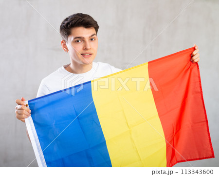 Happy young man holding flag of Romania against unicoloured background 113343600
