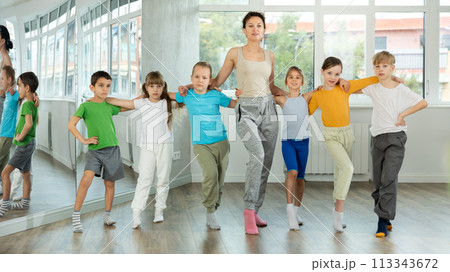 Smiling preteen children learning to dancing folk dance in row in studio 113343672