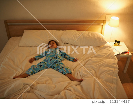 Boy, bed and rest for night, sleeping and tired with fatigue and peace. Child, dreaming and exhausted with pyjamas, dark and bedroom with lamp for serene childhood at home or house for calm kid Boy, bed and rest for night, sleeping and tired with fatigue and peace. Child, dreaming and exhausted with pyjamas, dark and bedroom with lamp for serene childhood at home or house for calm kid 113344437