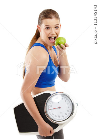 Portrait of woman, apple and scale in studio background for measurement, smile and excited for results of diet. Female person, body and care for calories target, weight loss and fruit to detox 113345143