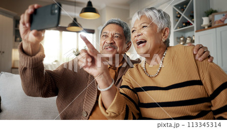 Senior couple, selfie and happy on sofa, hug or talking for choice, check post and point for photography in home. Elderly woman, man and laugh with profile profile, web blog and social media on couch 113345314