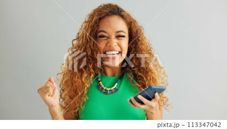 Excited woman, winner and phone with good news for lottery, prize or promotion on a gray studio background. Happy female person dancing with smile and mobile smartphone for celebration or success 113347042
