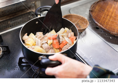 シチューを作るためじゃがいもと人参と玉葱と鶏肉を炒めるシニア女性 シチューを作るためじゃがいもと人参と玉葱と鶏肉を炒めるシニア女性 113347343