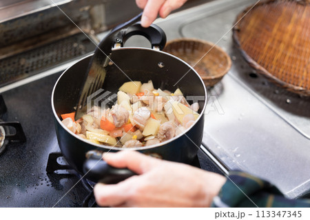 シチューを作るためじゃがいもと人参と玉葱と鶏肉を炒めるシニア女性 シチューを作るためじゃがいもと人参と玉葱と鶏肉を炒めるシニア女性 113347345