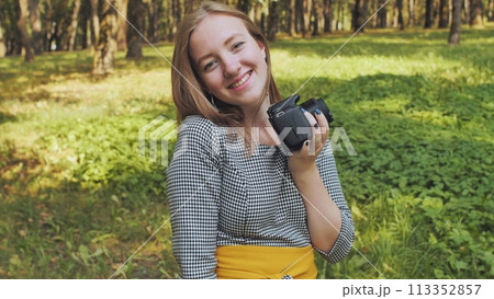 A young girl photographer with a camera poses in the park. 113352857