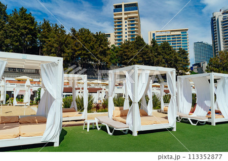 Luxury VIP beach with lounge canopy beach beds on green lawn. City resort. Hotel buildings on background 113352877