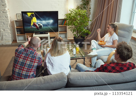 Friends, sport fans meeting at home, sitting on couch in living room on daytime and watching online football match translation. Friends, sport fans meeting at home, sitting on couch in living room on daytime and watching online football match translation. 113354121