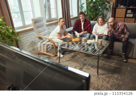 Game discussion. Friends, men and women sitting in living room at home and watching online football match translation. Game discussion. Friends, men and women sitting in living room at home and watching online football match translation. 113354126