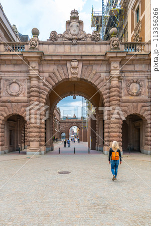 A woman approaches the grand gates of the Swedish Parliament House, Riksdagshuset, located in Stockholm, capturing the essence of historic and political significance. A woman approaches the grand gates of the Swedish Parliament House, Riksdagshuset, located in Stockholm, capturing the essence of historic and political significance. 113356266