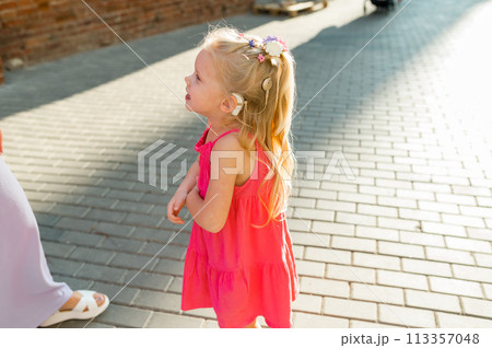 Child girl with hearing aid cochlear implant in pink dress having fun on summer street. Aid for the treatment of deafness and hearing loss in humans. Copy space Child girl with hearing aid cochlear implant in pink dress having fun on summer street. Aid for the treatment of deafness and hearing loss in humans. Copy space 113357048