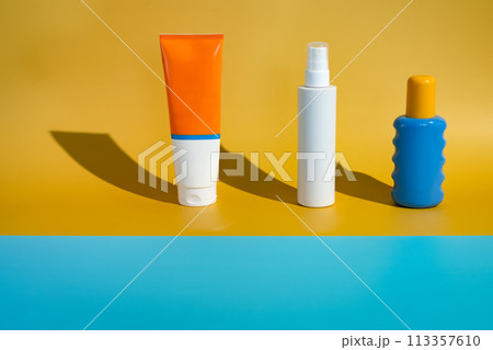 Different blank sunscreen packaging bottles on minimalist beach of yellow and blue paper in direct sunlight. Summer skin protection mockup template Different blank sunscreen packaging bottles on minimalist beach of yellow and blue paper in direct sunlight. Summer skin protection mockup template 113357610