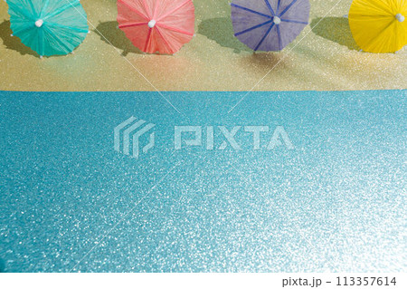 Abstract beach with glitter paper sand and water and cocktail umbrellas. Summer aesthetic mockup template background on a tropical beach holiday Abstract beach with glitter paper sand and water and cocktail umbrellas. Summer aesthetic mockup template background on a tropical beach holiday 113357614
