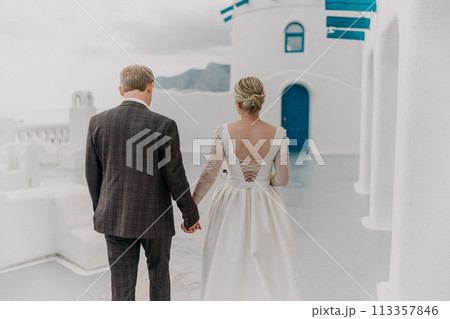A bride and groom are walking down a path in front of a blue door. The bride is wearing a white dress and the groom is wearing a suit. Scene is romantic and happy. 113357846