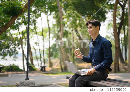 Portrait of attractive businessman sitting on a park bench and working with laptop 113359092