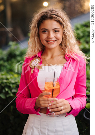 Beautiful young woman hold alcoholic cocktail in hands. Bride to be. Woman with curly hair drink aperol spritz Beautiful young woman hold alcoholic cocktail in hands. Bride to be. Woman with curly hair drink aperol spritz 113360209