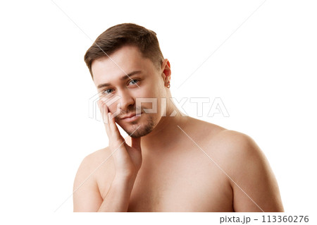 Portrait of shirtless bearded young handsome man looking at camera and touching his face against white studio background. Portrait of shirtless bearded young handsome man looking at camera and touching his face against white studio background. 113360276