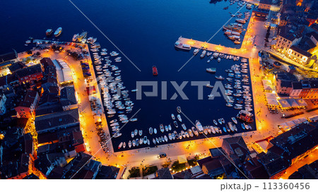 Birds eye view of the evening city during sunset. Aerial photography. Lights on lanterns on dusk. The ships are in the bay. Tiled roofs of houses in the old town. Rovinj, Croatia - April 7, 2024 Birds eye view of the evening city during sunset. Aerial photography. Lights on lanterns on dusk. The ships are in the bay. Tiled roofs of houses in the old town. Rovinj, Croatia - April 7, 2024 113360456