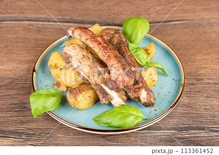Freshly baked pork ribs with potatoes and seasonings on a plate with basil leaves. 113361452