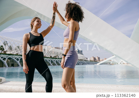 Happy female friends doing gesture of sport shake hand after exercising outside 113362140