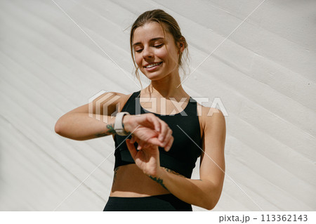 Smiling woman in sportswear looking on smartwatch after training. Outdoor sports in the morning 113362143