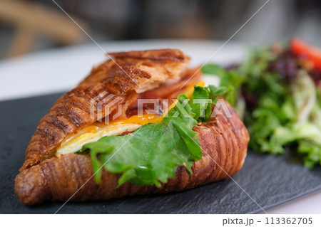 4K Breakfast Scene. A woman is eating a croissant with bacon and scrambled eggs at breakfast. High quality 4k footage 113362705