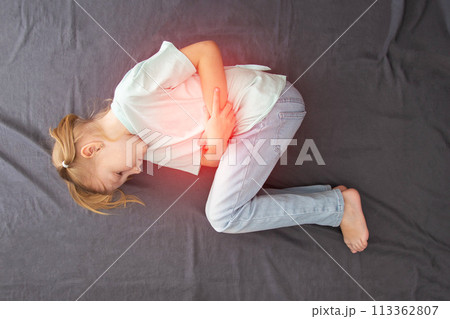 A seven-year-old girl lies and holds her lower abdomen with pain and inflammation of the bladder. Concept of bacterial cystitis in children, hypothermia. Pediatric urology. Frequent urination, view 113362807