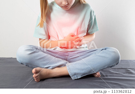 A little girl sits and holds her sore red stomach with her hands. Cognition of liver and gallbladder diseases in children. Cholelithiasis, biliary dyskinesia, cholecystitis 113362812
