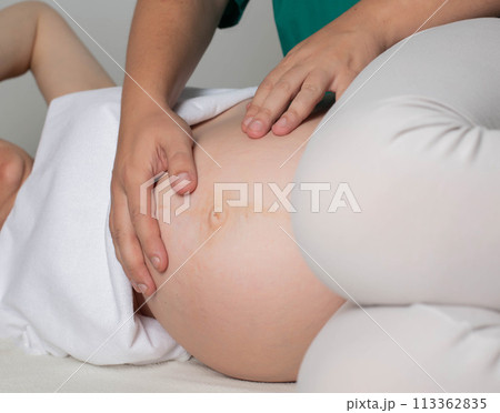 An osteopathic doctor palpates the belly of a pregnant girl in the third trimester. Preparation before childbirth. Osteopathy and pregnancy, therapeutic 113362835