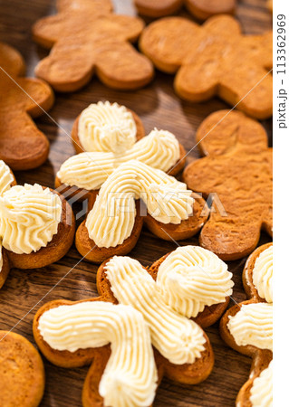 Making gingerbread man cookie sandwiches filled with eggnog buttercream, arrayed on a rustic wooden table, ideal for heartfelt Christmas gifting. 113362969