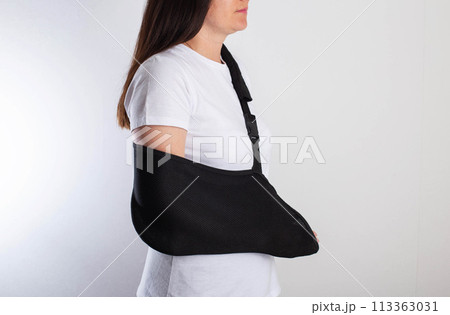 A girl in white with a fixing black bandage on her arm after an injury, a fracture of the radius and a sprain. Arm support bandage, hand immobilization A girl in white with a fixing black bandage on her arm after an injury, a fracture of the radius and a sprain. Arm support bandage, hand immobilization 113363031